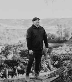 Winemaker Matt Taylor standing and smiling in Ink Grade Howell Mountain vineyards, black and white