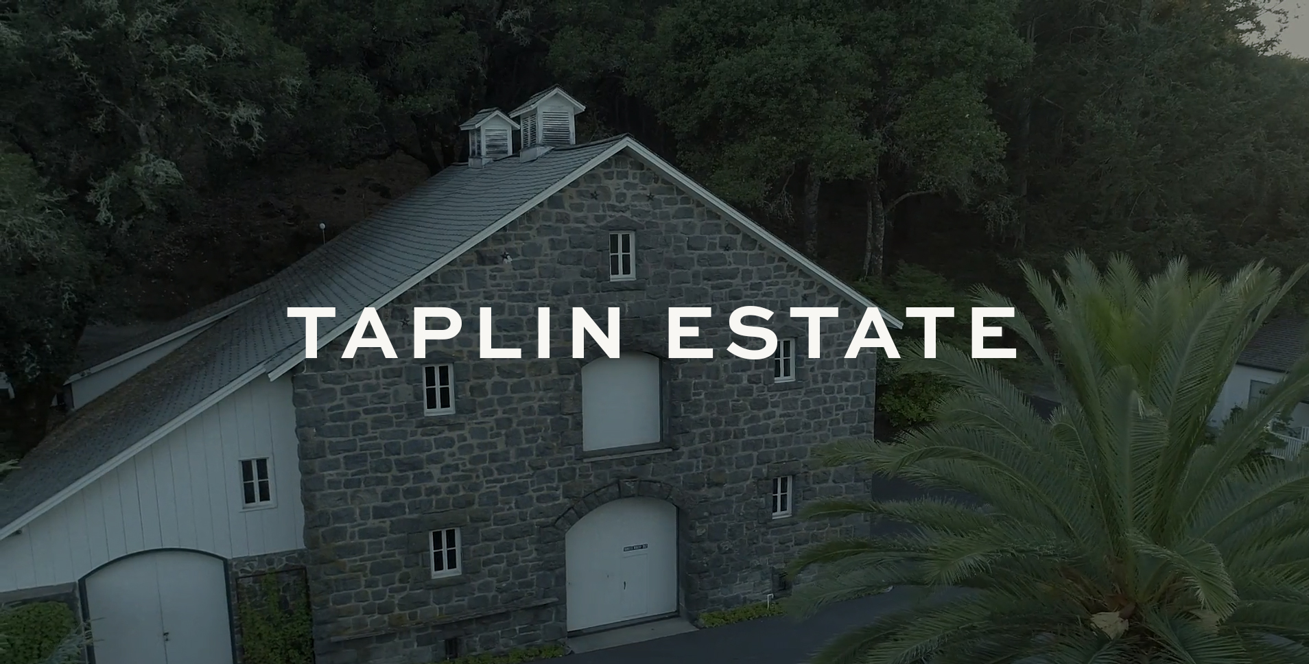 Exterior shot of stone wine cellar with white door with text Taplin Estate superimposed