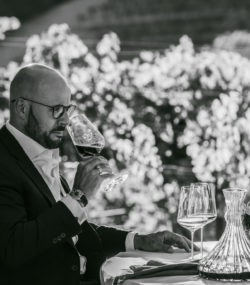 Carlton McCoy smells a glass of wine at a table in the Ink Grade vineyard black and white