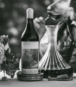 Ink Grade Andosol Zinfandel bottle next to decanter with Matt Taylor sniffing wine glass in background black and white