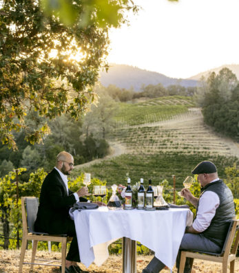Matt Taylor and Carlton McCoy cheers over table in Ink Grade Vineyard with wine bottles and decanters