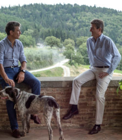 Filippo Mazzei and Francesco Mazzei leaning on short wall conversing with the estate in the background and a dog in the foreground